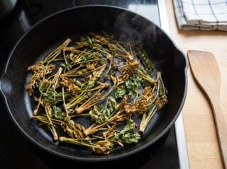Fanes de carotte et de radis saisies a sec dans une cocotte en fonte brulante, deja dorees par endroits, sans matiere grasse